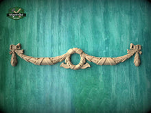 Load image into Gallery viewer, A decorative wooden carving of a bow and ribbon is displayed against a green wooden background.