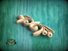 Load image into Gallery viewer, A wooden carving of a stylized flower or leaf design is displayed against a teal-colored background.