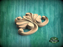 Load image into Gallery viewer, A wooden carving of a stylized flower or plant design is displayed against a teal background.