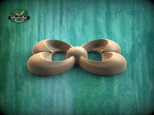 Load image into Gallery viewer, A wooden sculpture in the shape of a flower or bow, with curved petals and a round center, is displayed against a green background.