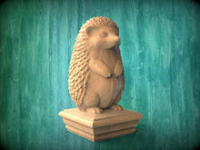 Load image into Gallery viewer, A wooden hedgehog statue stands on a pedestal against a green background.