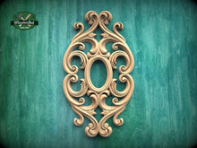 Load image into Gallery viewer, an ornate, carved wooden piece with an oval shape and intricate scrollwork, set against a green background.