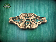Load image into Gallery viewer, a decorative wooden piece with intricate scrollwork and floral designs, set against a green wooden background.