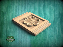 Load image into Gallery viewer, A wooden plaque with a carved flower design is displayed against a green textured background.