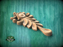 Load image into Gallery viewer, A wooden carving of a stylized leaf or flower-like shape is displayed against a green background.