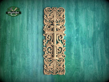 Load image into Gallery viewer, a decorative wooden cross with intricate floral and scrollwork designs, mounted on a green wooden surface.
