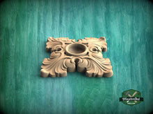 Load image into Gallery viewer, A decorative wooden piece with an ornate, floral design sits on a green textured background.