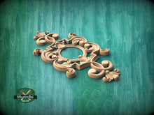 Load image into Gallery viewer, A decorative wooden carving with intricate scrollwork and floral elements is displayed against a green wooden background.