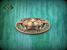 Load image into Gallery viewer, a decorative wooden emblem with a stylized face and wings, set against a green wooden background.