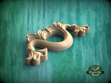 Load image into Gallery viewer, A wooden carving of a stylized flower or plant with intricate details is displayed against a green background.