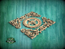 Load image into Gallery viewer, a decorative wooden carving with intricate scrollwork and a central motif, set against a green wooden background.