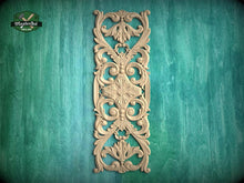 Load image into Gallery viewer, an ornate, carved wooden panel with intricate floral and scroll designs, mounted on a green wooden surface.