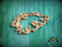Load image into Gallery viewer, an ornate, carved wooden frame with intricate scrollwork and floral designs, set against a green background.