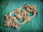 a carved wooden piece with intricate scrollwork and floral designs, set against a green background.
