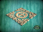 a decorative wooden carving with intricate scrollwork and a central motif, set against a green background.