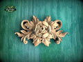 A decorative wooden carving of a flower with leaves is displayed against a green background.