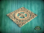 a decorative wooden carving with intricate scrollwork and a central motif, set against a green background.