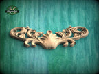 A decorative wooden carving with intricate scrollwork is displayed against a green wooden background.