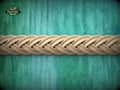 A close-up view of a braided wooden object, possibly a piece of furniture or a decorative item, set against a textured green background.