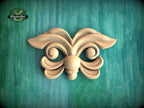 A wooden carving of a butterfly-like design is displayed against a green background.