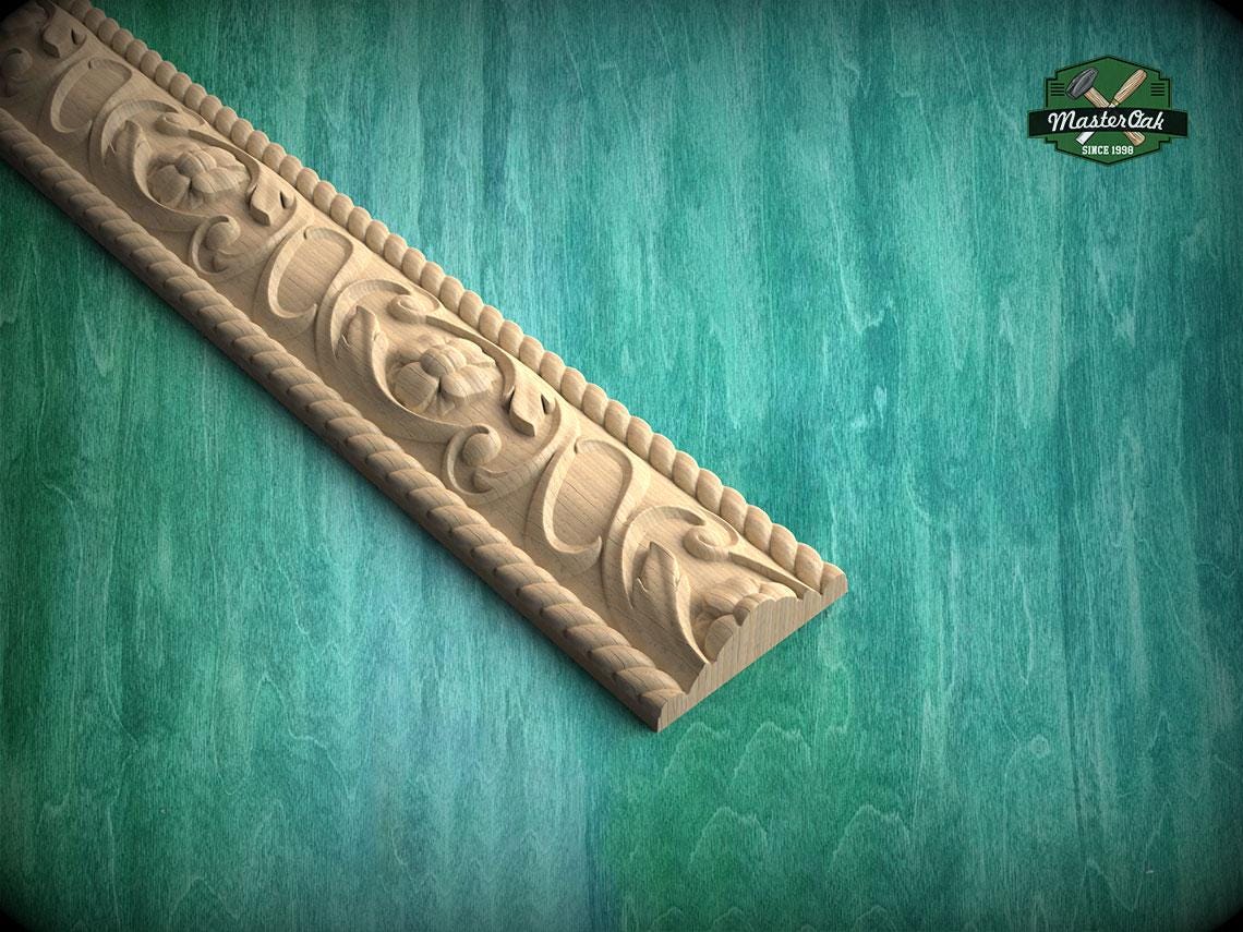 A decorative wooden molding with intricate floral designs is displayed against a green textured background.