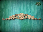 A decorative wooden carving in the shape of a fan or scroll is displayed against a teal-colored background.