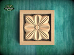 A wooden relief in the shape of a flower is displayed in a square frame against a green background.