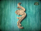 A decorative wooden carving in the shape of a flower or leaf is displayed against a green textured background.