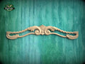 A decorative wooden carving of a floral design is displayed against a green textured background.