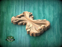 Load image into Gallery viewer, A wooden carving of a stylized leaf or flower design is displayed against a green background.
