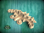 A wooden carving of a decorative leaf or flower design is displayed against a green background.