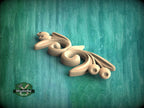 A wooden carving of a stylized flower or leaf design is displayed against a teal-colored background.