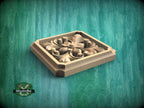 A square wooden carving with intricate floral designs sits on a green wooden surface.