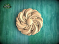 A wooden flower-shaped carving is displayed against a green background.