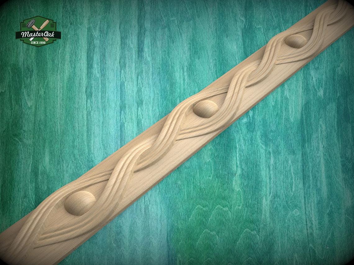 A decorative wooden trim with a wavy pattern and two circular elements is displayed against a green wooden background.