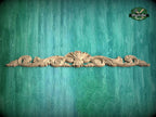 A decorative wooden carving with intricate scrollwork is displayed against a textured green background.