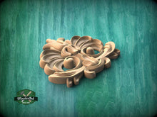 Load image into Gallery viewer, A wooden carving of a stylized flower or leaf design is displayed against a green background.
