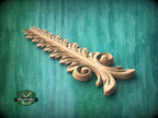 A decorative wooden leaf-like object with intricate curves and patterns, resting on a green textured background.