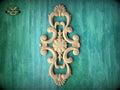 an ornate, carved wooden design with intricate scrollwork and floral elements, set against a green textured background.