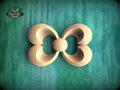A wooden carving of a stylized flower or butterfly shape is displayed against a green background.