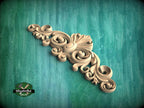 A decorative wooden carving with intricate swirls and curves is displayed against a teal background.