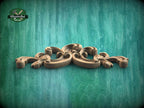 A decorative wooden carving with intricate scrollwork is displayed against a textured green background.