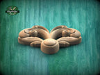 A wooden carving of a stylized flower or leaf design is displayed against a green background.