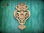 an ornate, carved wooden piece with intricate scrollwork and floral designs, mounted on a green wooden surface.