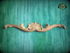 A decorative wooden carving with a shell-like design is displayed against a teal-colored background.