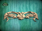 A decorative wooden carving with intricate floral and leaf-like patterns is displayed against a green wooden background.