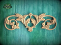a decorative wooden carving with intricate floral and scroll designs, set against a green background.