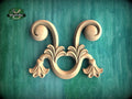 A decorative wooden carving with two curved, flower-like elements is displayed against a green background.