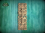 a decorative wooden cross with intricate floral and scrollwork designs, mounted on a green wooden surface.
