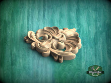 Load image into Gallery viewer, A wooden carving with intricate floral and leaf-like designs sits on a green textured background.
